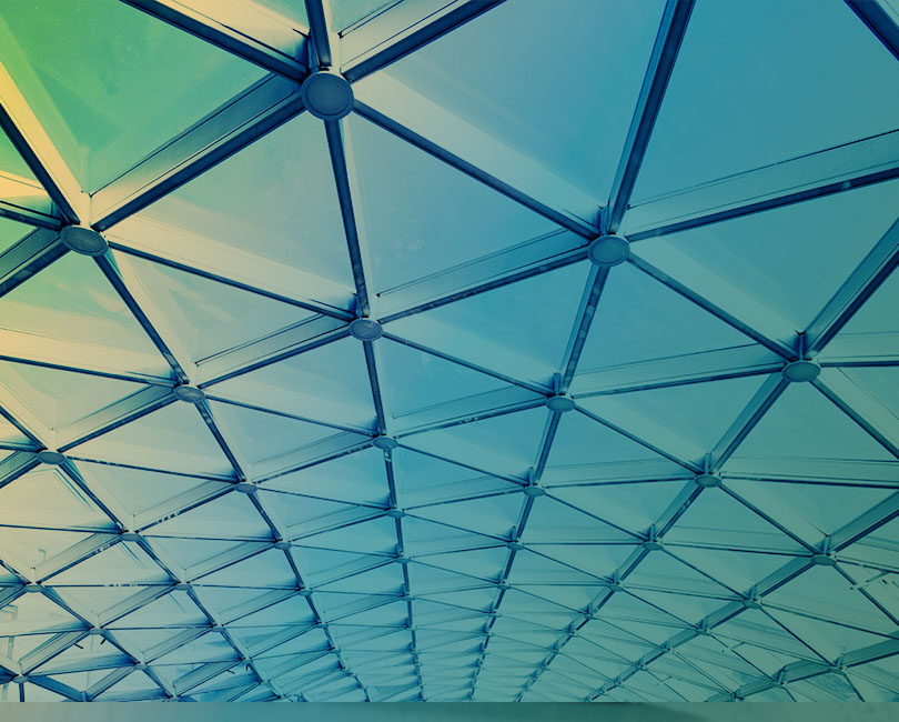 Geometric glass ceiling with a grid of intersecting metal beams and circular joints, tinted blue and yellow from sunlight—an abstract, modern architectural pattern that inspires ideas for creating a resilient AEC firm.
