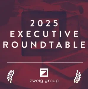 Red graphic with the text "2025 Executive Roundtable" in bold letters. Below is the Zweig Group logo and name, with laurel leaf graphics on either side. Background shows faint images of a laptop and workspace.