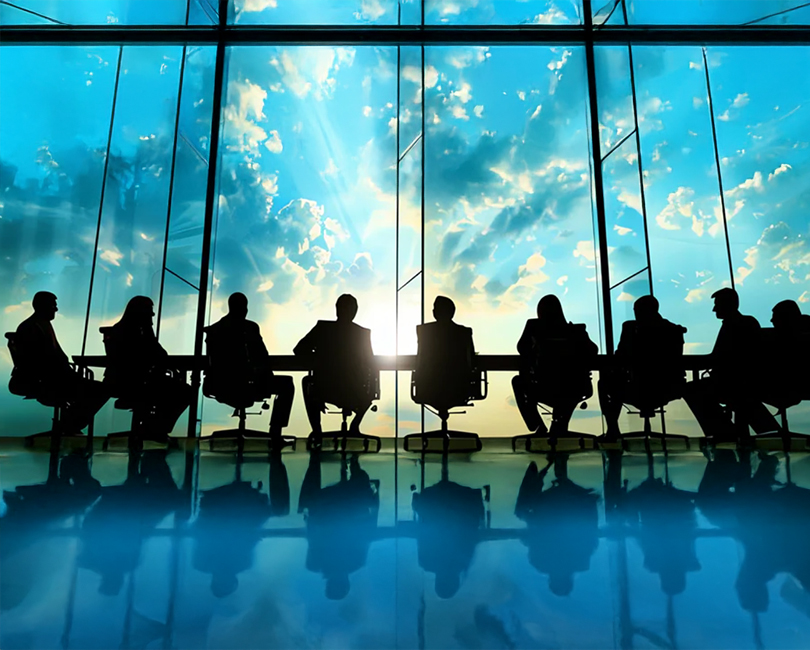 Silhouettes of people sitting around a long conference table in front of large windows, with sunlight and clouds visible outside, creating a dramatic and reflective atmosphere.