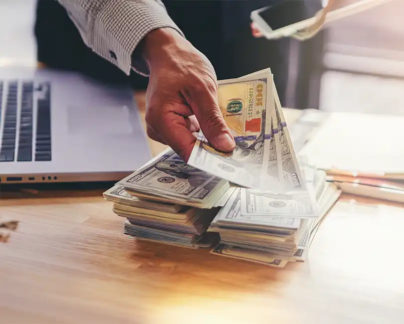 Graphic titled 'Bonus vs. Distribution: Optimizing Owner Compensation in AEC' featuring a close-up of a professional's hands counting a fan of $100 bills over a desk. The post is authored by Robert E. Jones, CPA, CPCM, and includes the Stambaugh Ness logo.