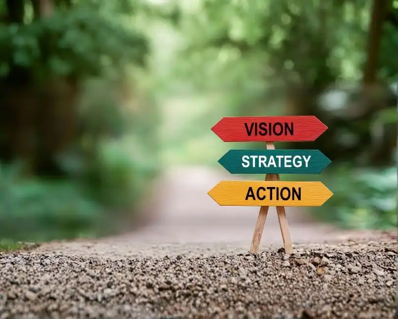 Stambaugh Ness blog feature graphic for "AEC Strategic Planning Priorities: What Are Firms Focusing On?" by Scott D. Butcher. The graphic features a wooden signpost with colorful arrows pointing to "VISION", "STRATEGY", and "ACTION" on a soft-focus forest background, transitioning to a dark gradient overlay at the bottom with the title text and the Stambaugh Ness logo.